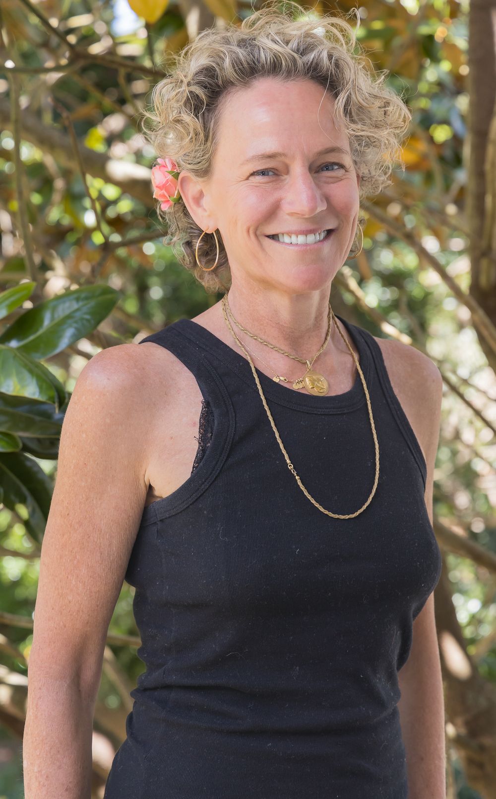 Portrait of someone in black tank top with gold necklace against natural background.
