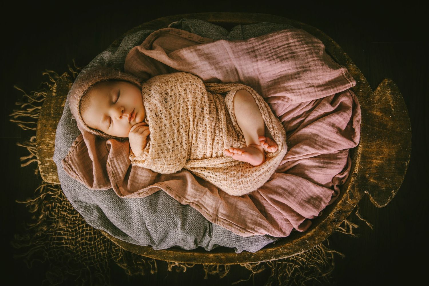 A newborn baby sleeping peacefully on pink fabric in a rustic basket.
