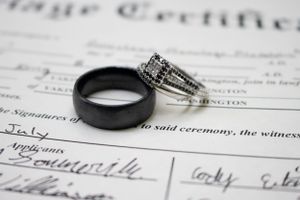 A black tungsten and diamond wedding ring set resting on a marriage certificate document.