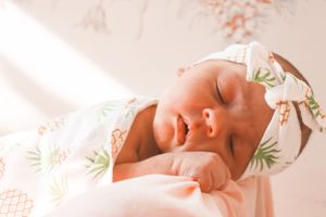 Peaceful newborn baby sleeping wrapped in pineapple print swaddle blanket with matching headband.