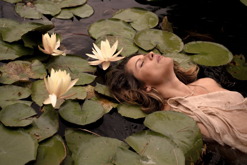 Artistic portrait among floating water lilies and lily pads in dark water.