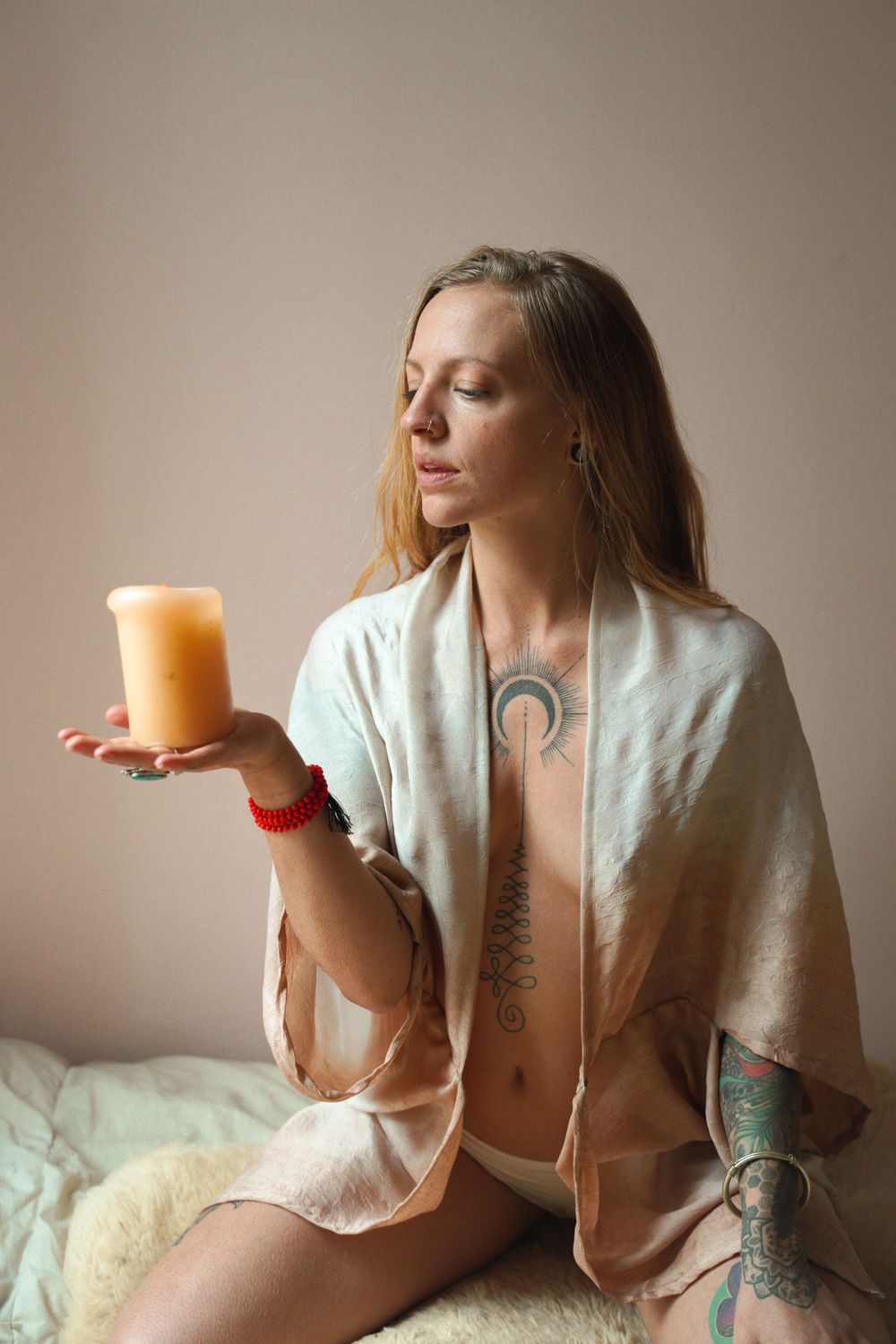 Artistic portrait with orange candle and light robe in minimalist setting.
