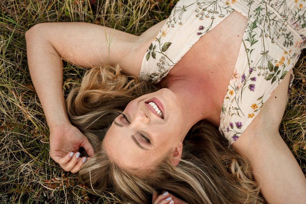 A joyful moment lying in grass wearing a floral dress while basking in natural sunlight.