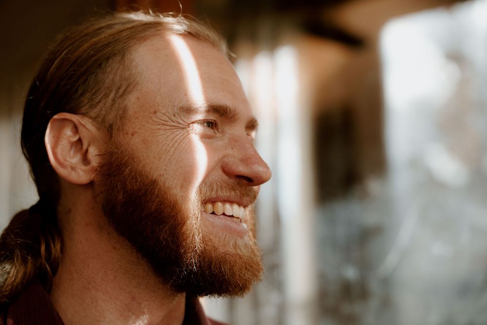A profile view of a bearded man smiling in warm sunlight.