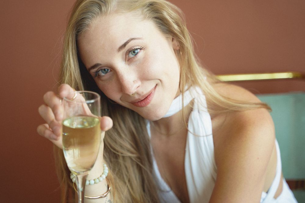 Joyful lifestyle portrait with white top and champagne glass against terracotta wall.