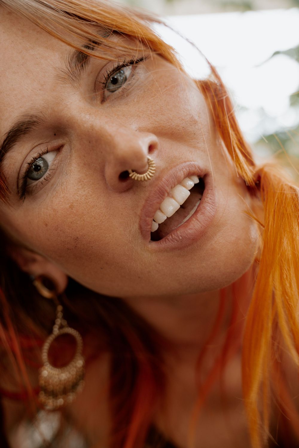 Close-up portrait with vibrant orange hair and bohemian jewelry.