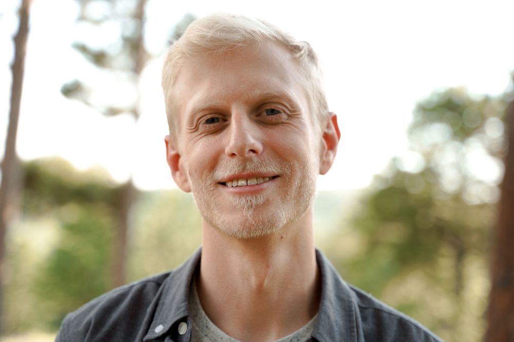 Warm sunlit portrait outdoors wearing dark button-up shirt.