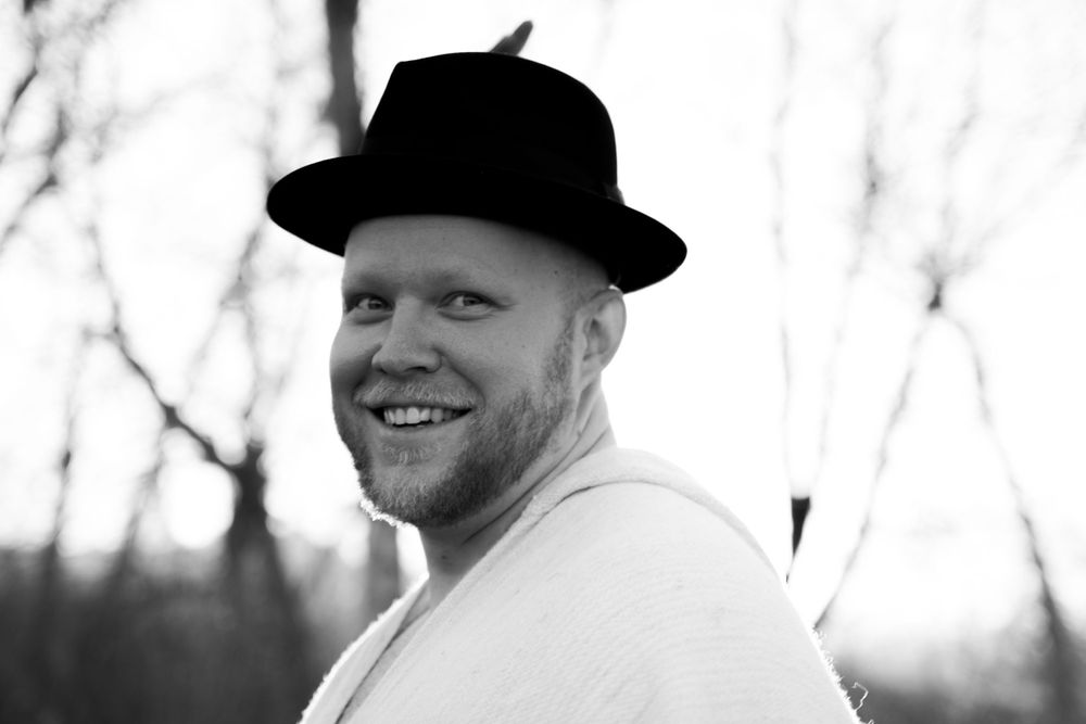 Black and white portrait of a person wearing a fedora hat and smiling.