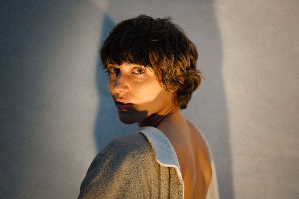 Artistic portrait with dramatic side lighting and short dark hair against neutral background.