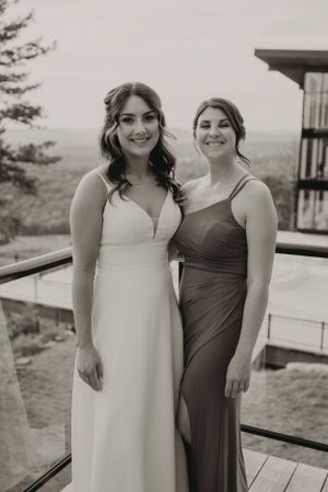 Two women in formal dresses pose on a balcony with mountain views.