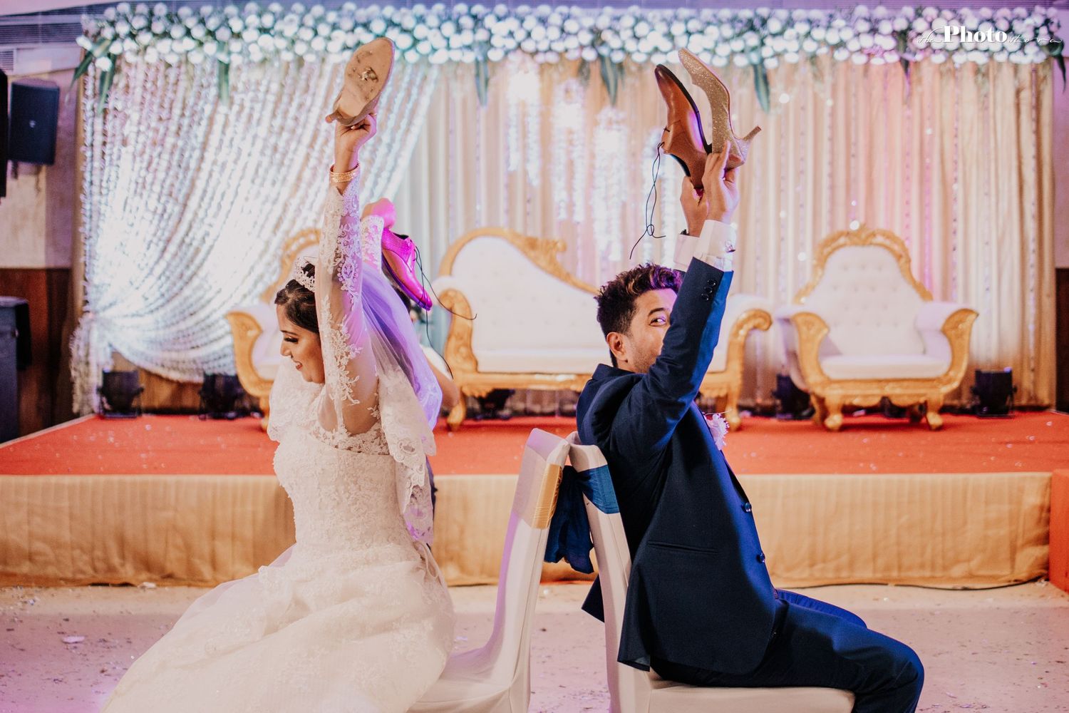 Wedding couple striking a playful pose with raised arms against a decorated backdrop.