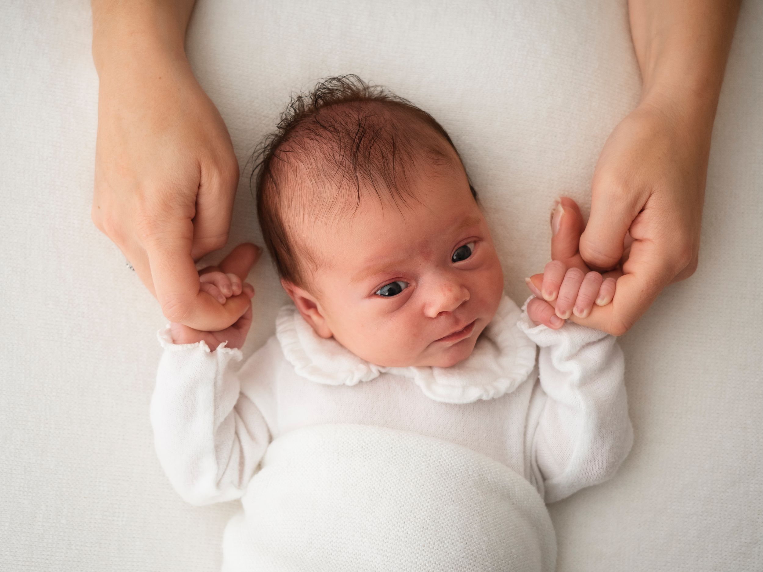 A newborn baby photoshoot in didcot, the baby is holding the mothers hands and looking at the camera