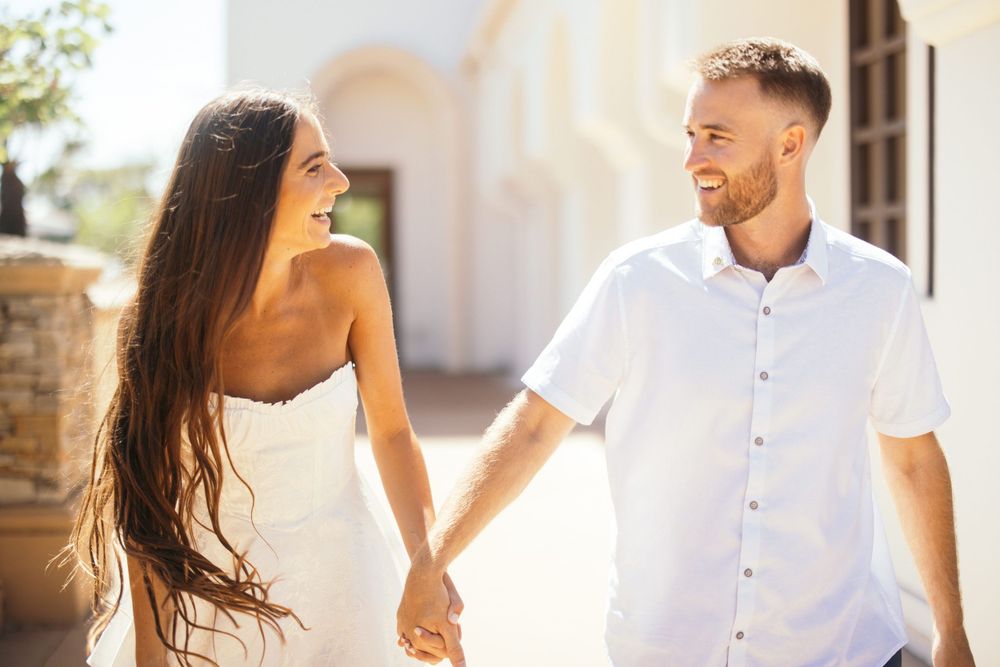 Sun-filled moment between couple walking along Mediterranean-style architecture.