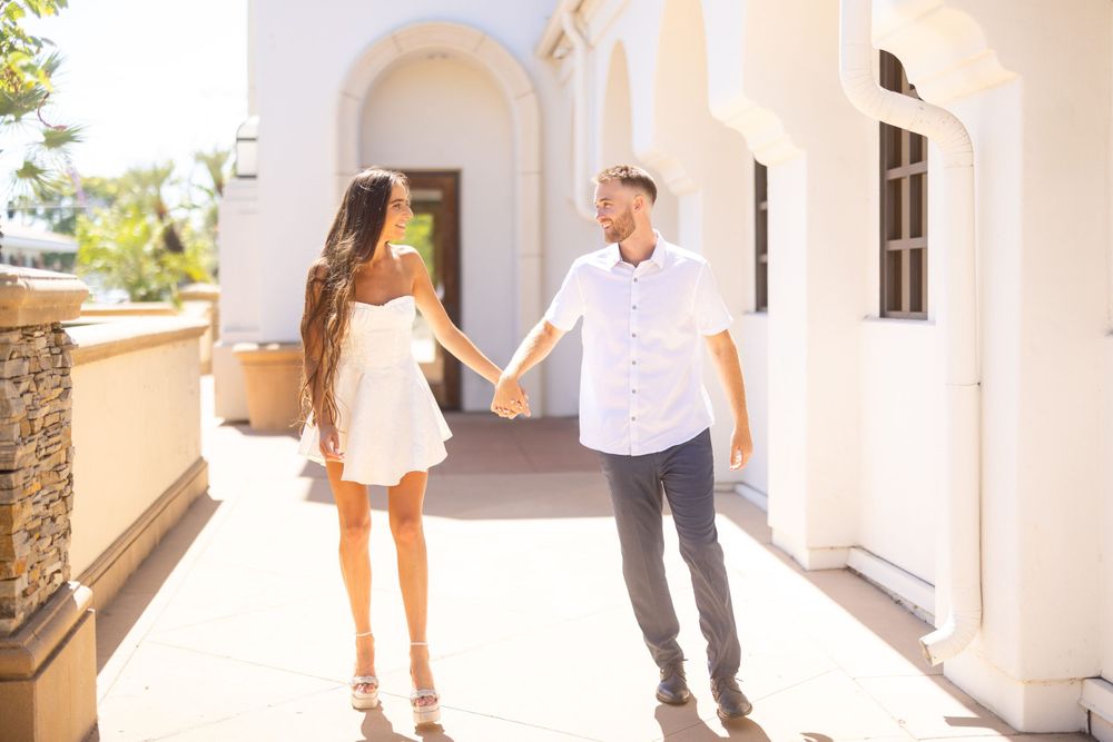 Playful couple holding hands while walking through a bright Mediterranean courtyard.