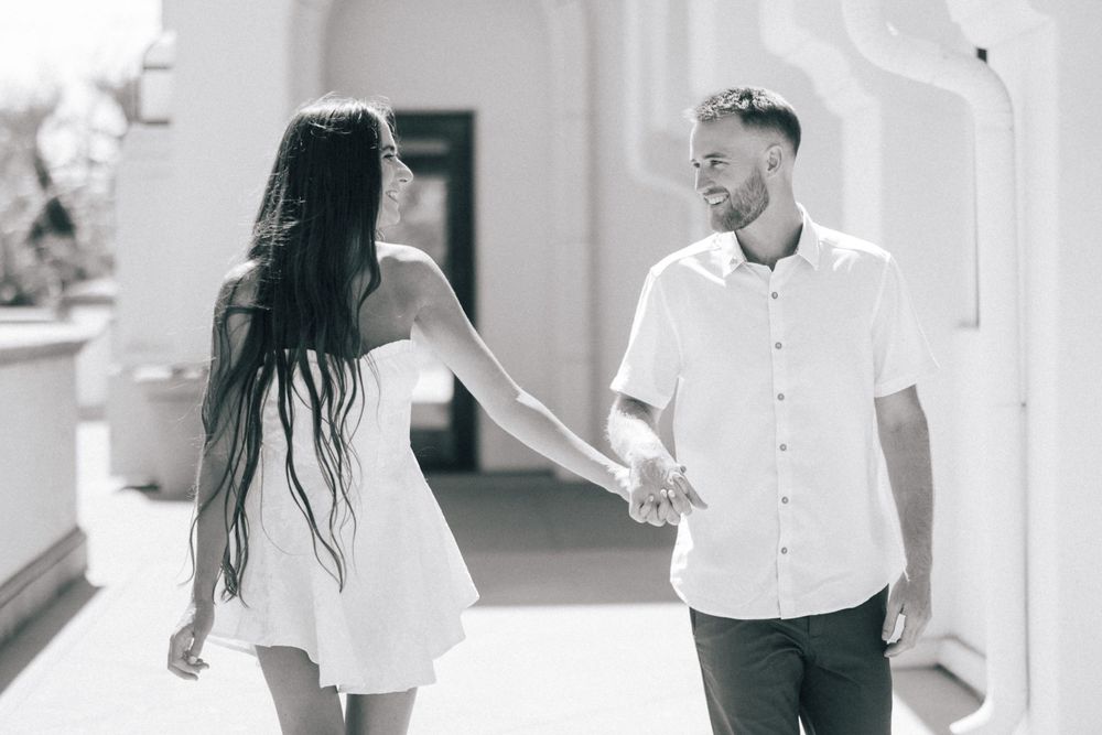 Black and white photo of couple walking through an elegant arched corridor.