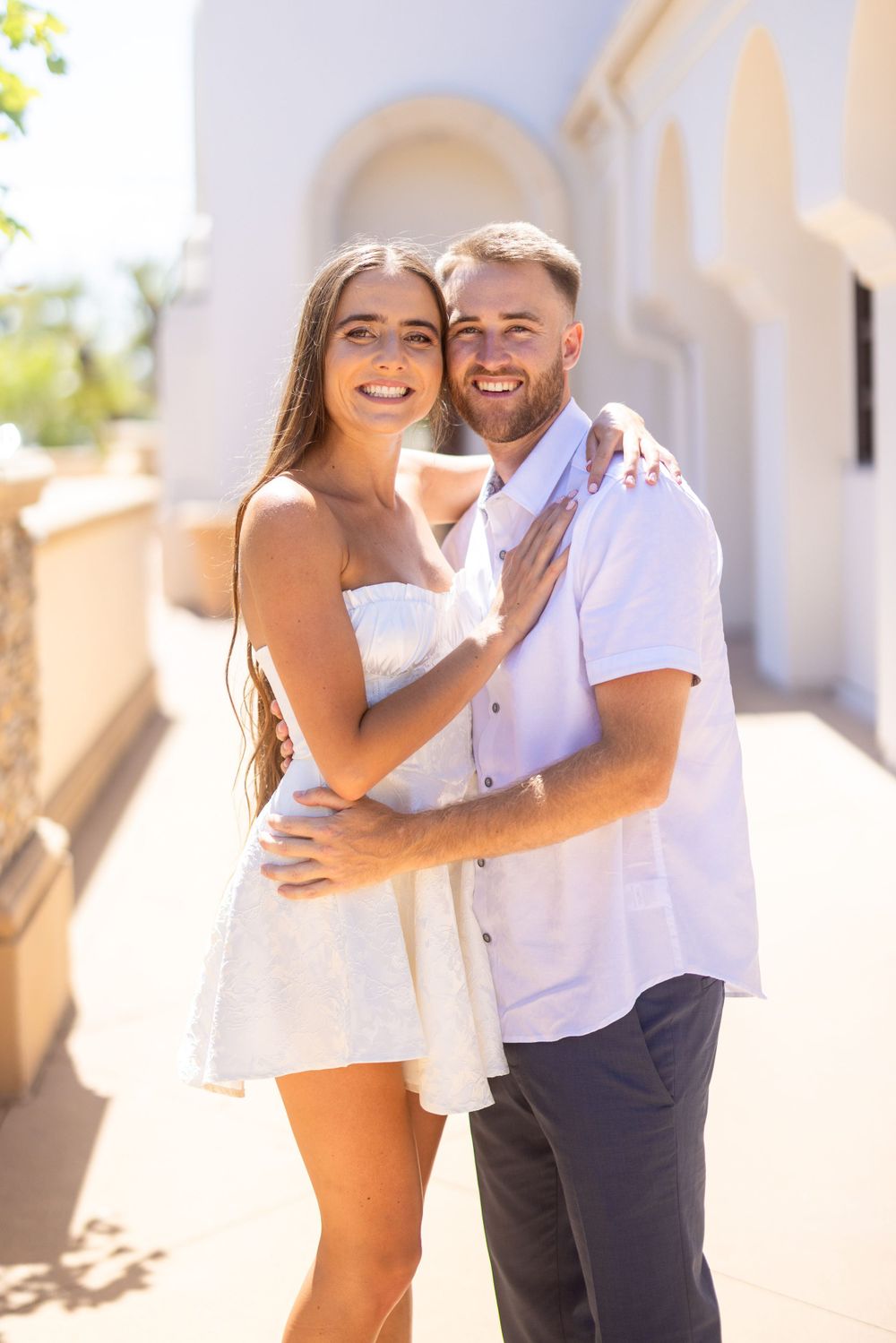 Sun-drenched portrait against white Mediterranean architecture on a summer day.