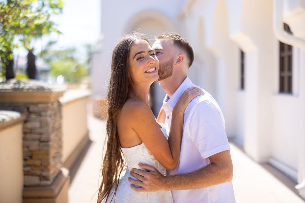 Intimate moment captured in bright sunlight along a Mediterranean-style walkway with white walls.