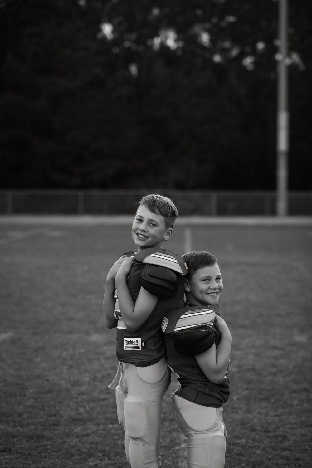 Two young athletes in football gear stand back-to-back on a field at night.