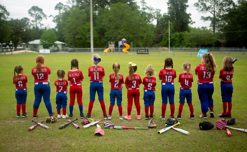 Youth softball team lined up on field showing uniform numbers on their backs.