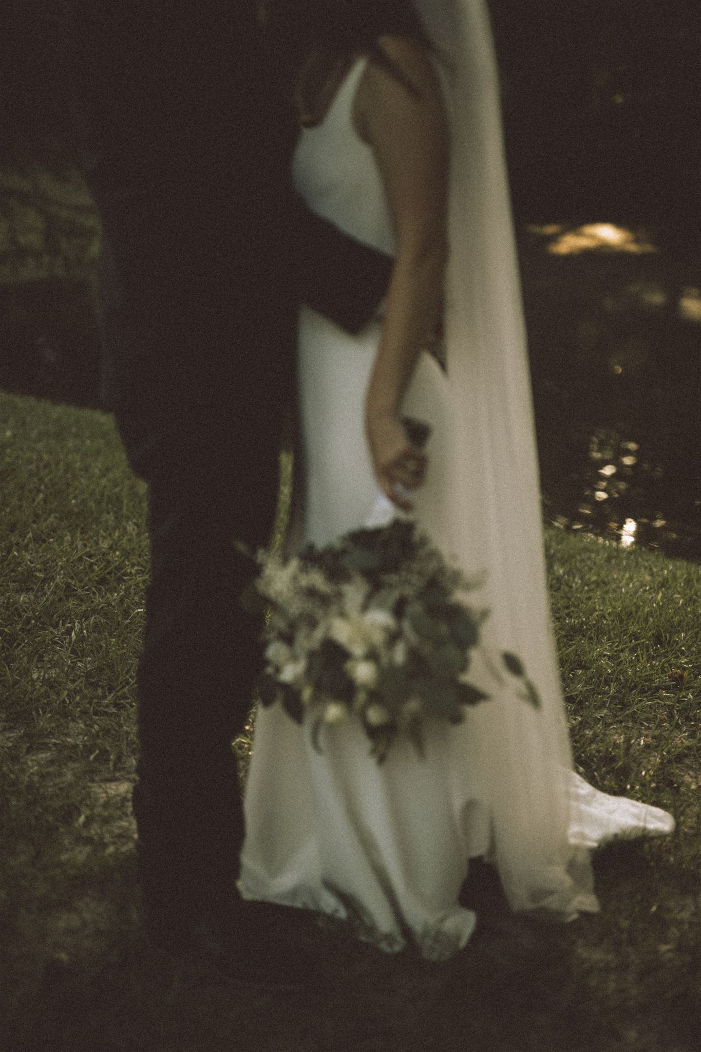 Close-up silhouette of wedding couple with flowing white dress and bouquet at dusk.