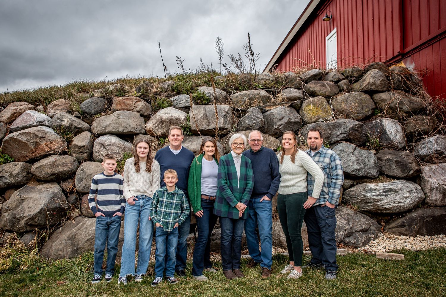 Group portrait against rock wall and red barn under cloudy sky.