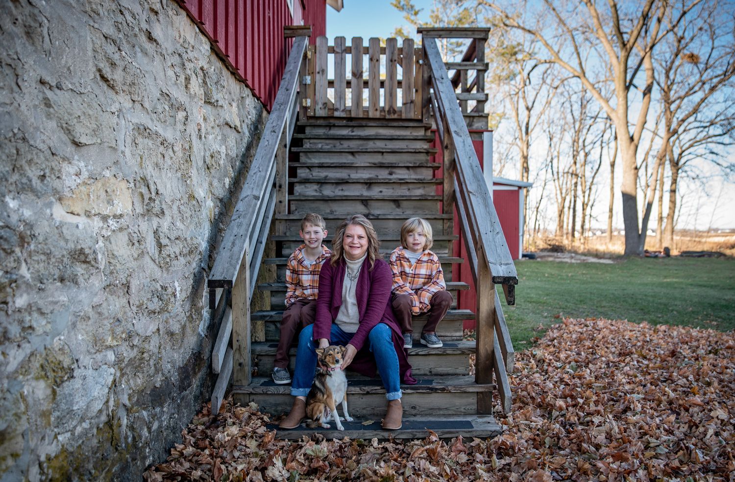 Rustic family portrait on wooden steps against stone wall of historic barn.