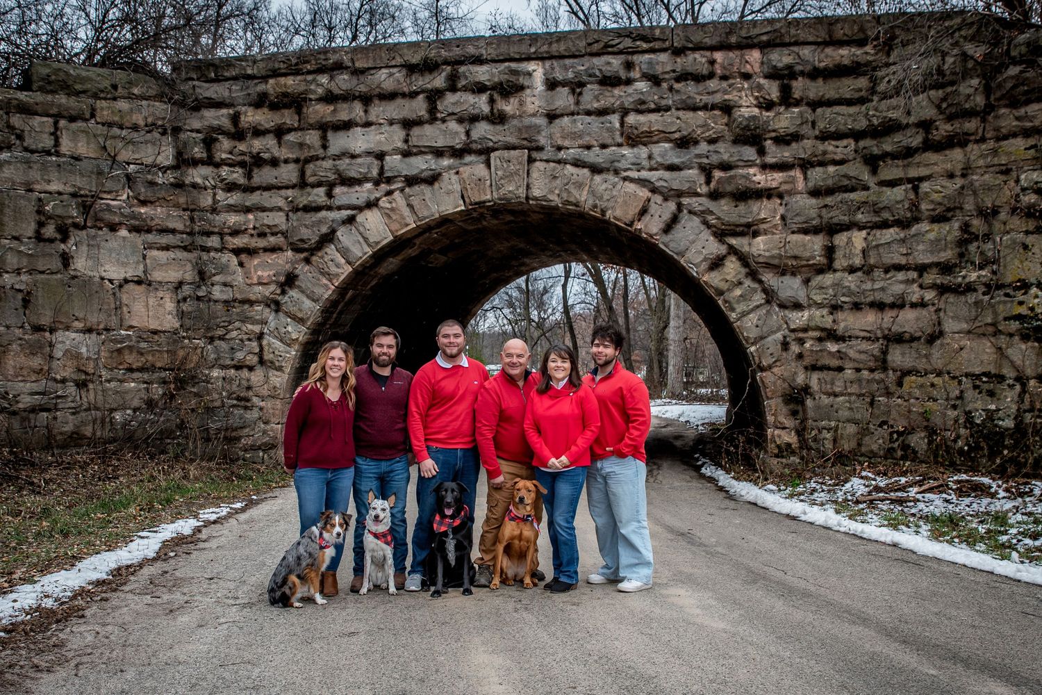 Winter family portrait beneath stone arch bridge with dogs.
