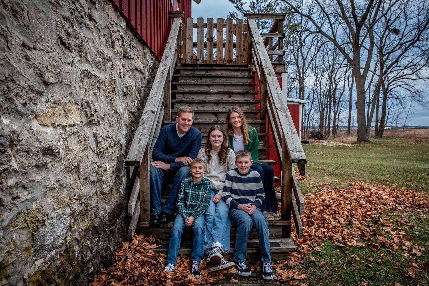 Family seated together on rustic stone steps with wooden railing surrounded by autumn leaves.