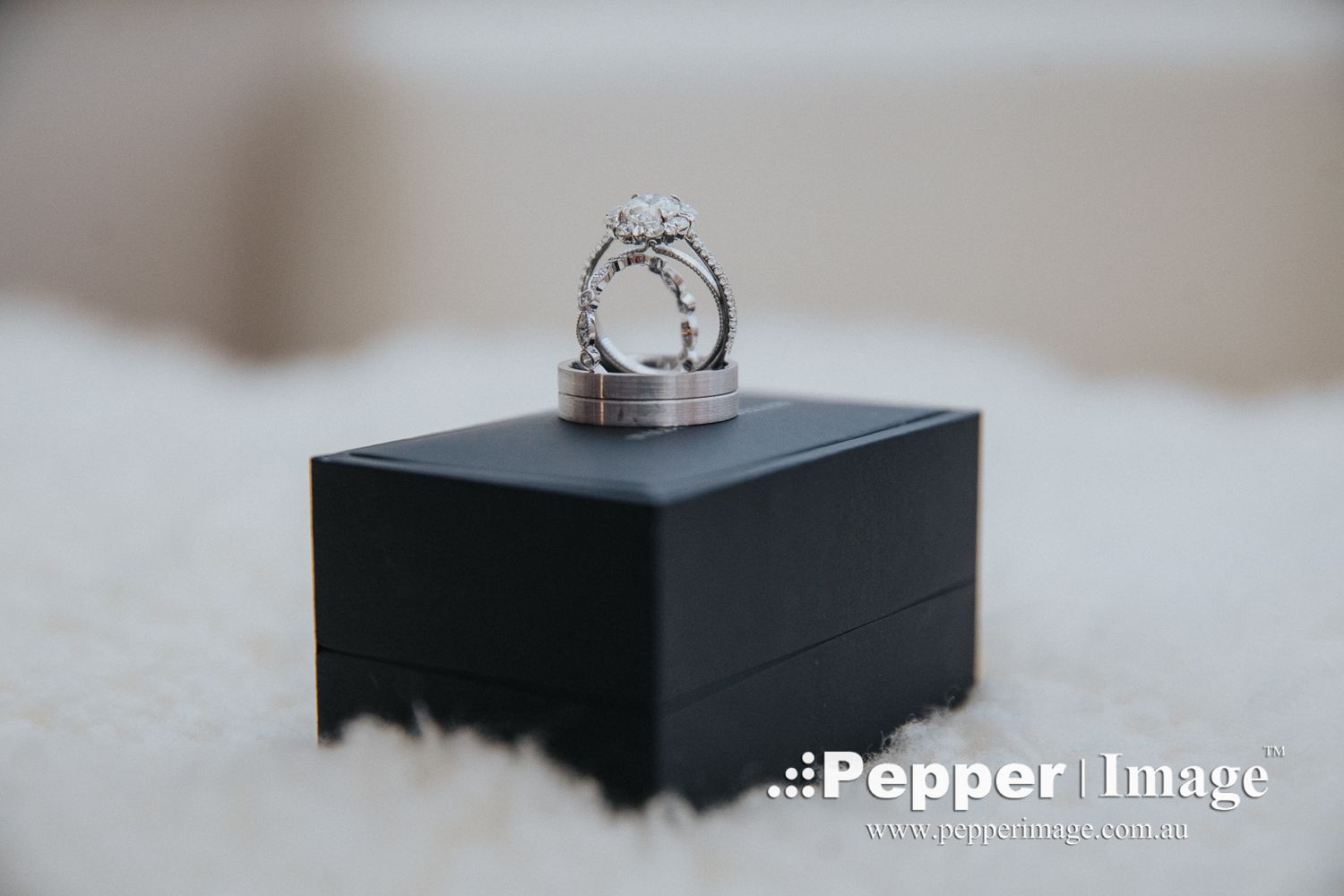 Diamond engagement ring and wedding bands displayed on a black jewelry box on white fur.