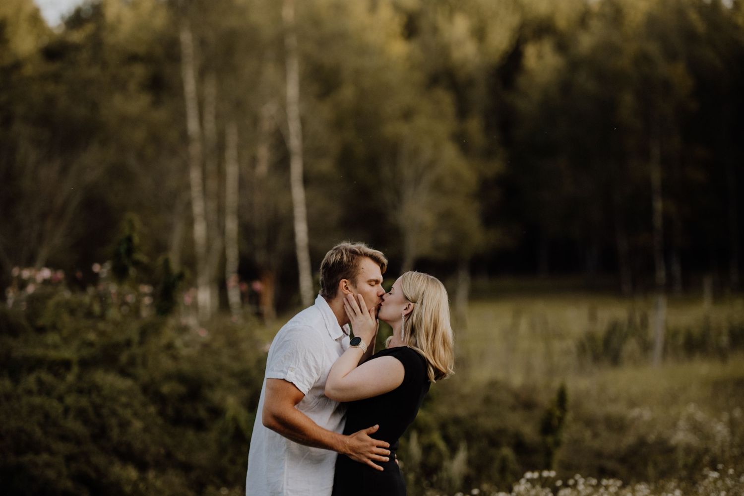 A romantic couple embracing in a golden-lit forest clearing at sunset.