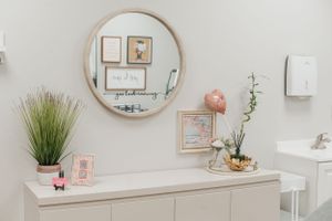 Modern minimalist vanity area with round mirror and decorative frames on light walls.