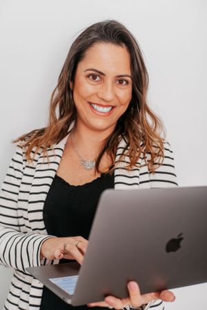 Professional in striped blazer working on MacBook laptop in bright setting.
