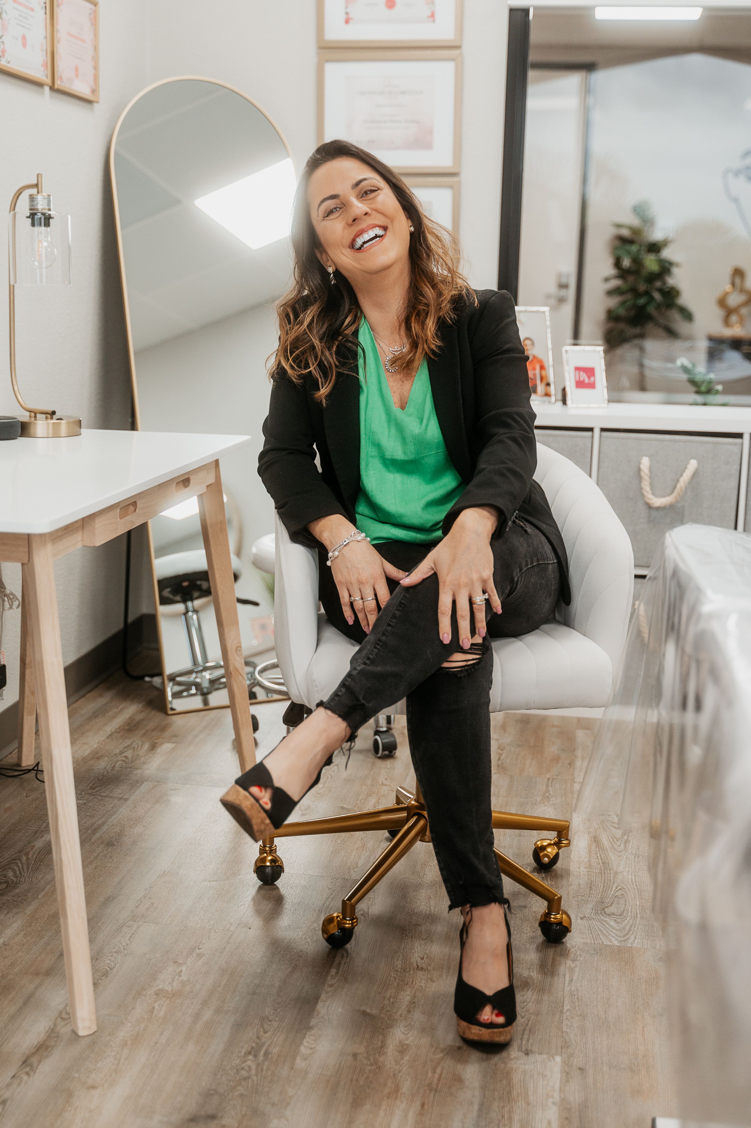 A professional sits cheerfully in an office chair wearing business attire with a green blouse.