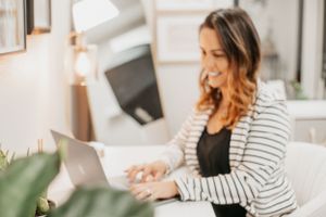 Professional working on laptop wearing black top and striped blazer in home office setting.