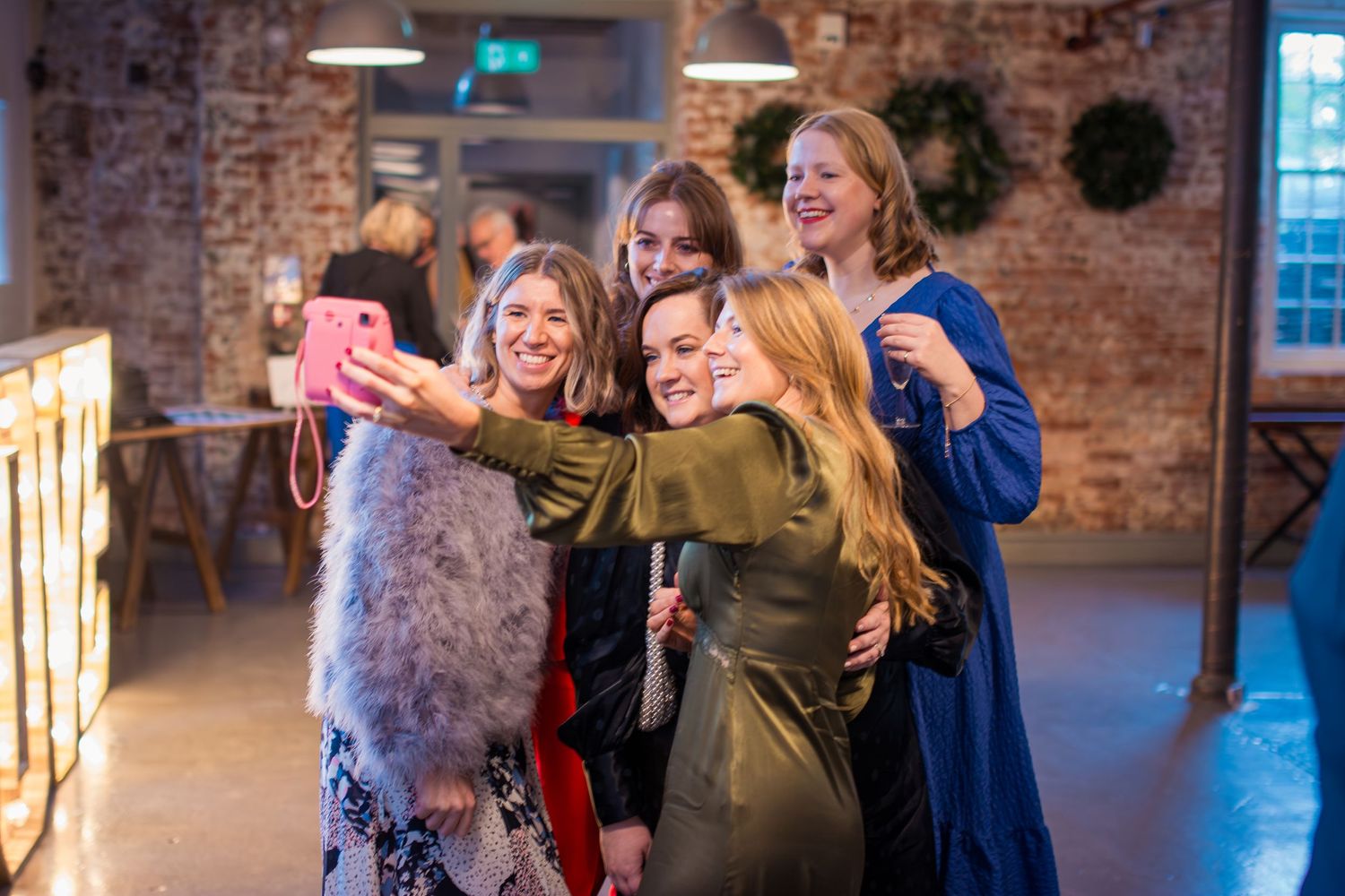 Group of friends taking selfies together in rustic brick venue with warm lighting.