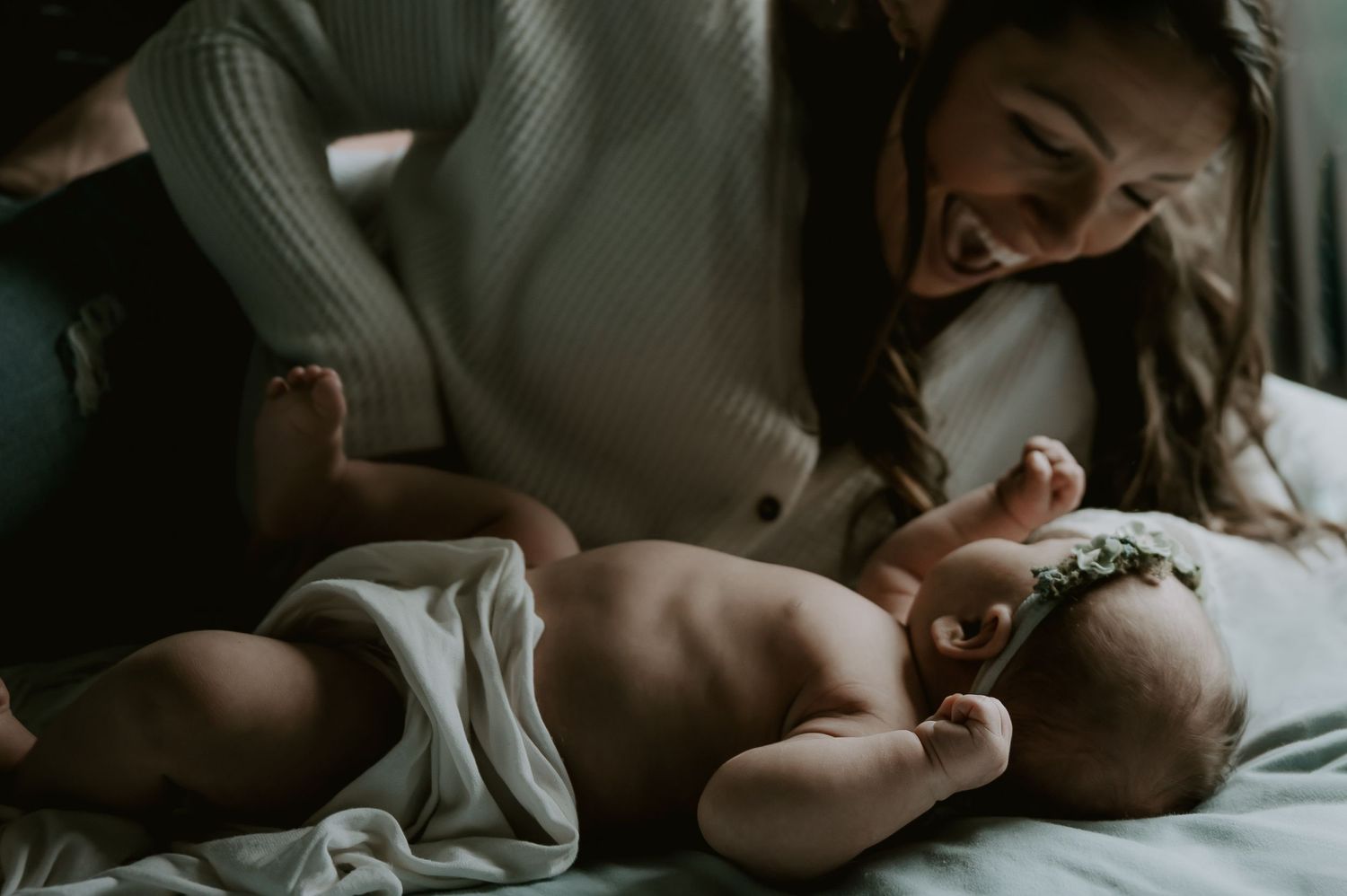 A tender moment with a newborn baby lying on white bedding while being gently touched.