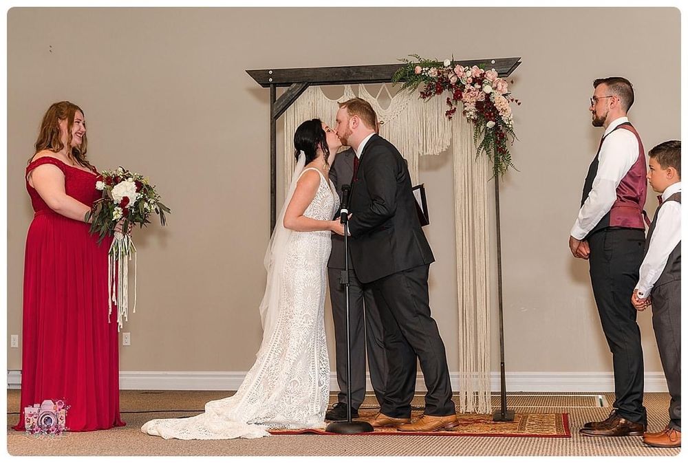 Wedding ceremony under floral arch with burgundy and neutral decor in intimate setting.