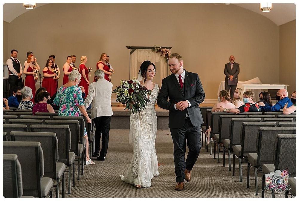 Wedding procession down church aisle with bridal party and guests looking on.