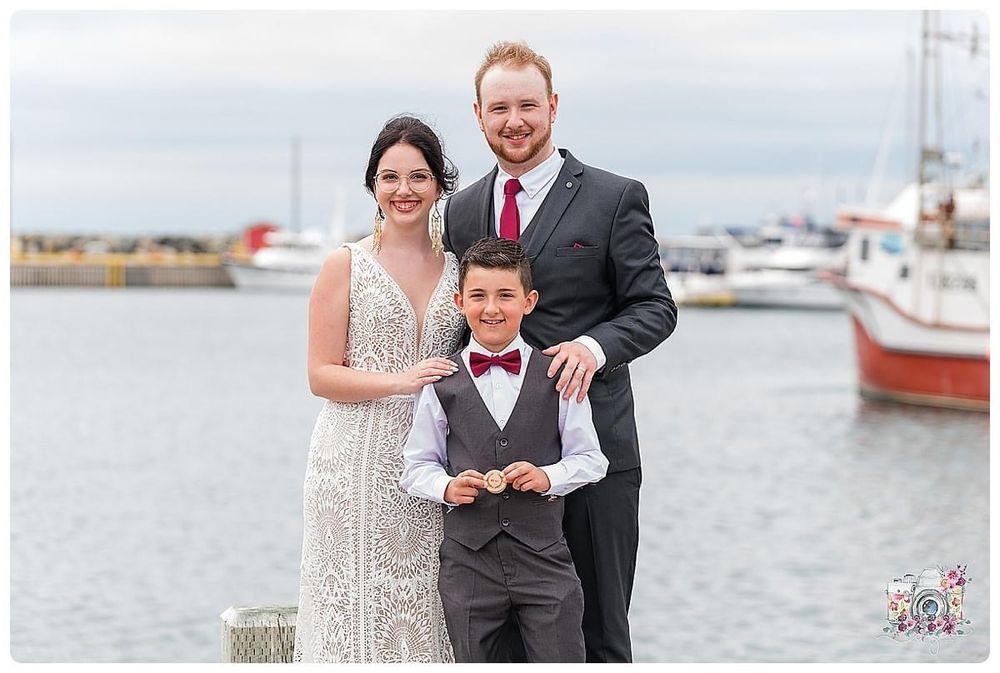 A formal portrait on a dock with boats in the background during a coastal wedding celebration.