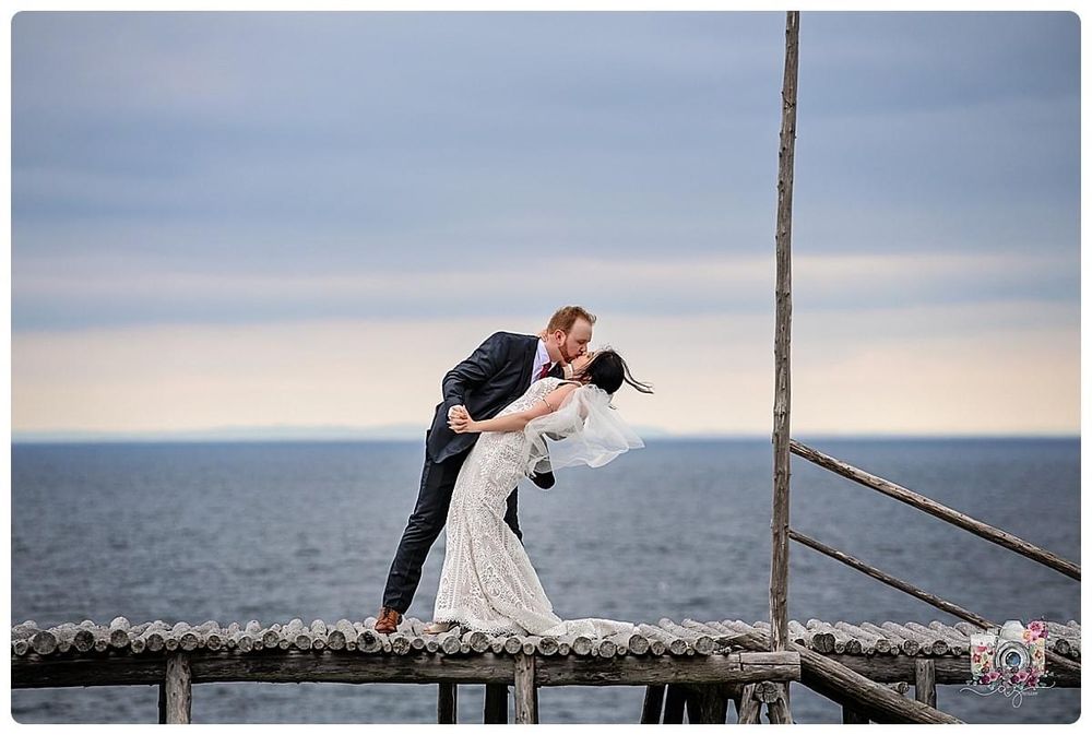 Dramatic wedding pose on a wooden pier overlooking the ocean at dusk.