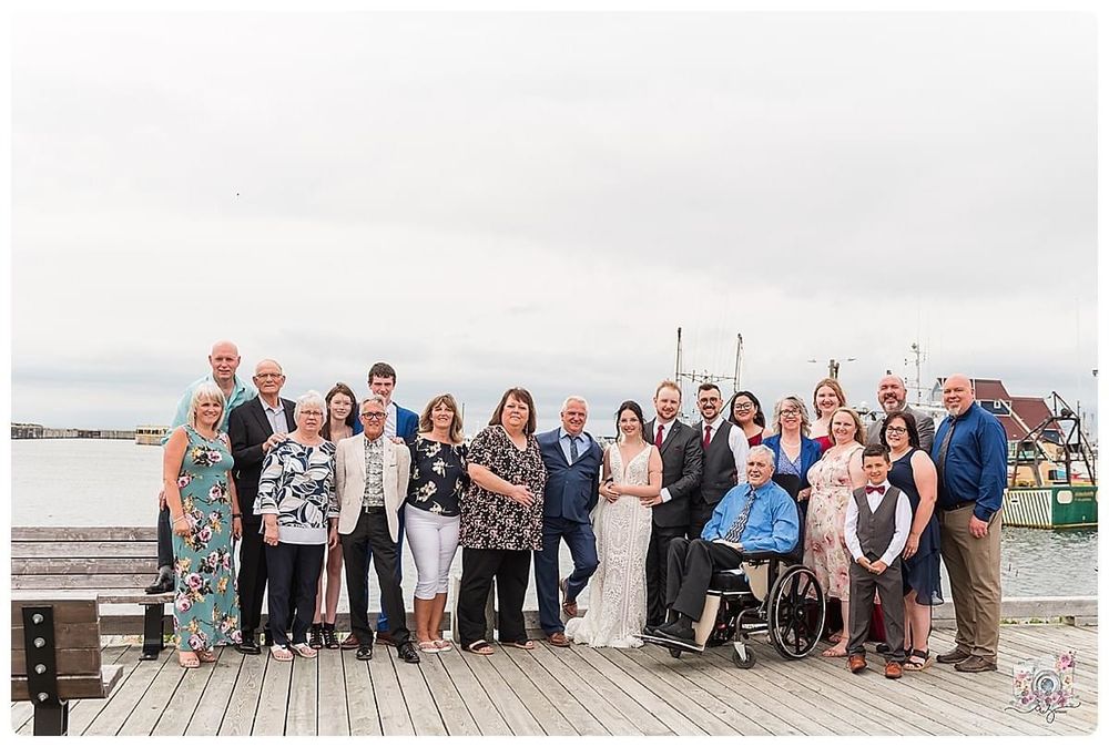 Group photo of wedding guests gathered on wooden dock by water.