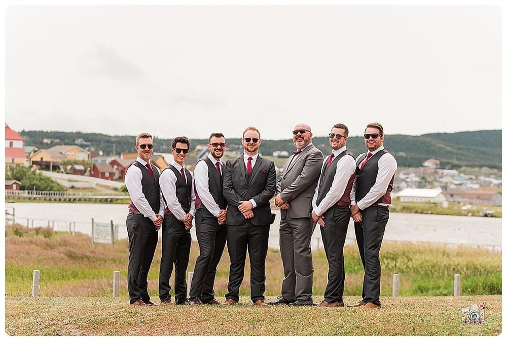Groomsmen in grey suits and vests pose together on grassy hillside.