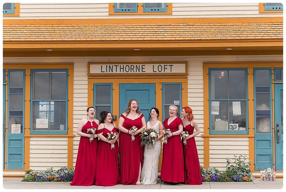 Bridal party in red dresses poses in front of yellow Linthorne Loft building.