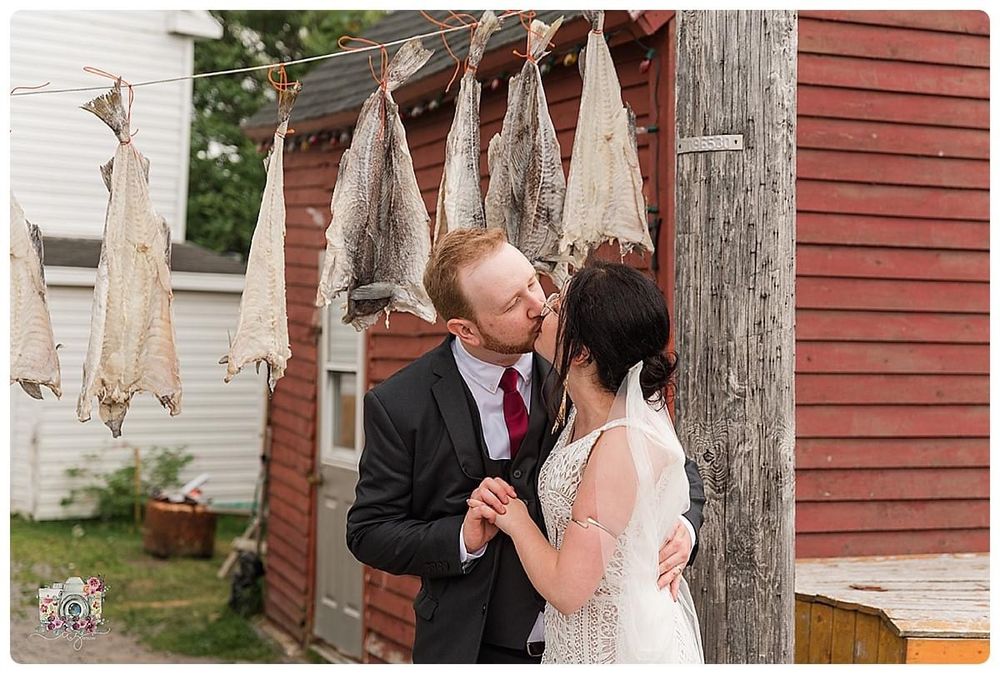 Romantic moment shared between couple near rustic red barn with fish hanging to dry.