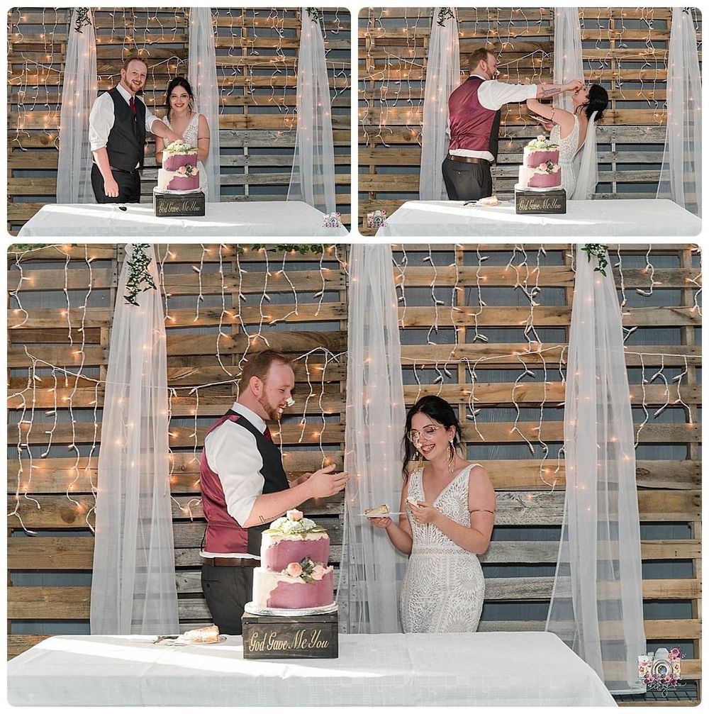 Couple shares a heartfelt moment cutting their pink wedding cake against a rustic wooden backdrop with white draping.