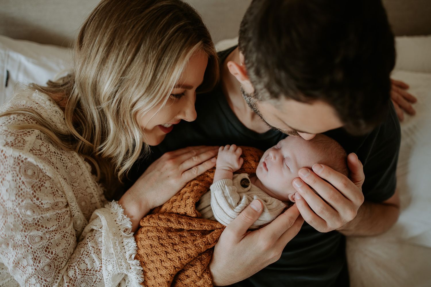 A tender family moment as parents gaze lovingly at their newborn swaddled in a knitted blanket.