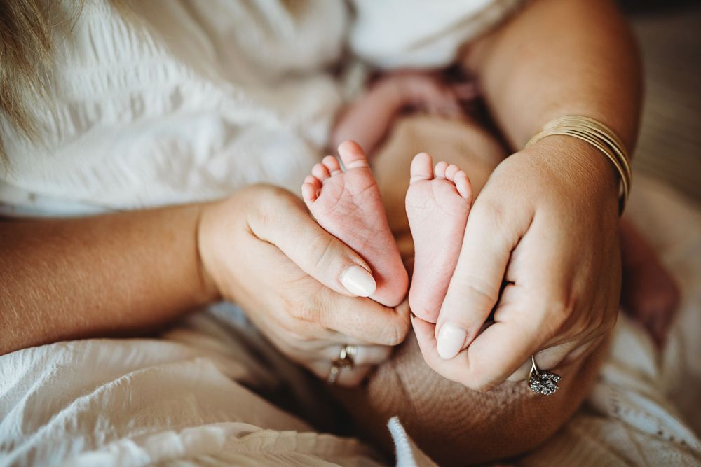 Close-up of mother's hands gently cradling tiny newborn baby feet with gold bracelet and ring visible.