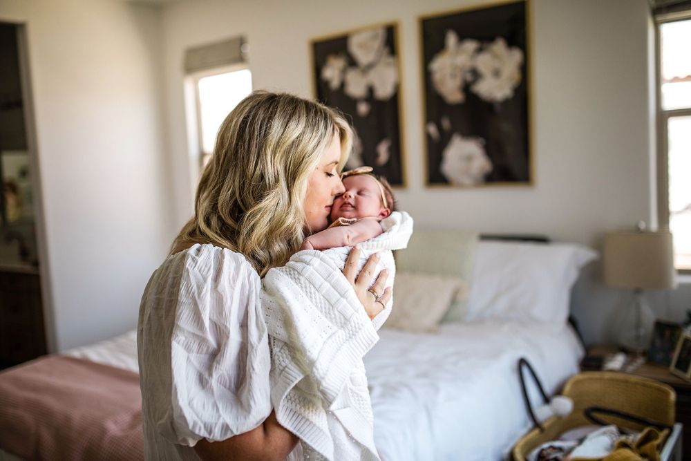 Mother lovingly kisses her newborn baby in a bright bedroom setting.