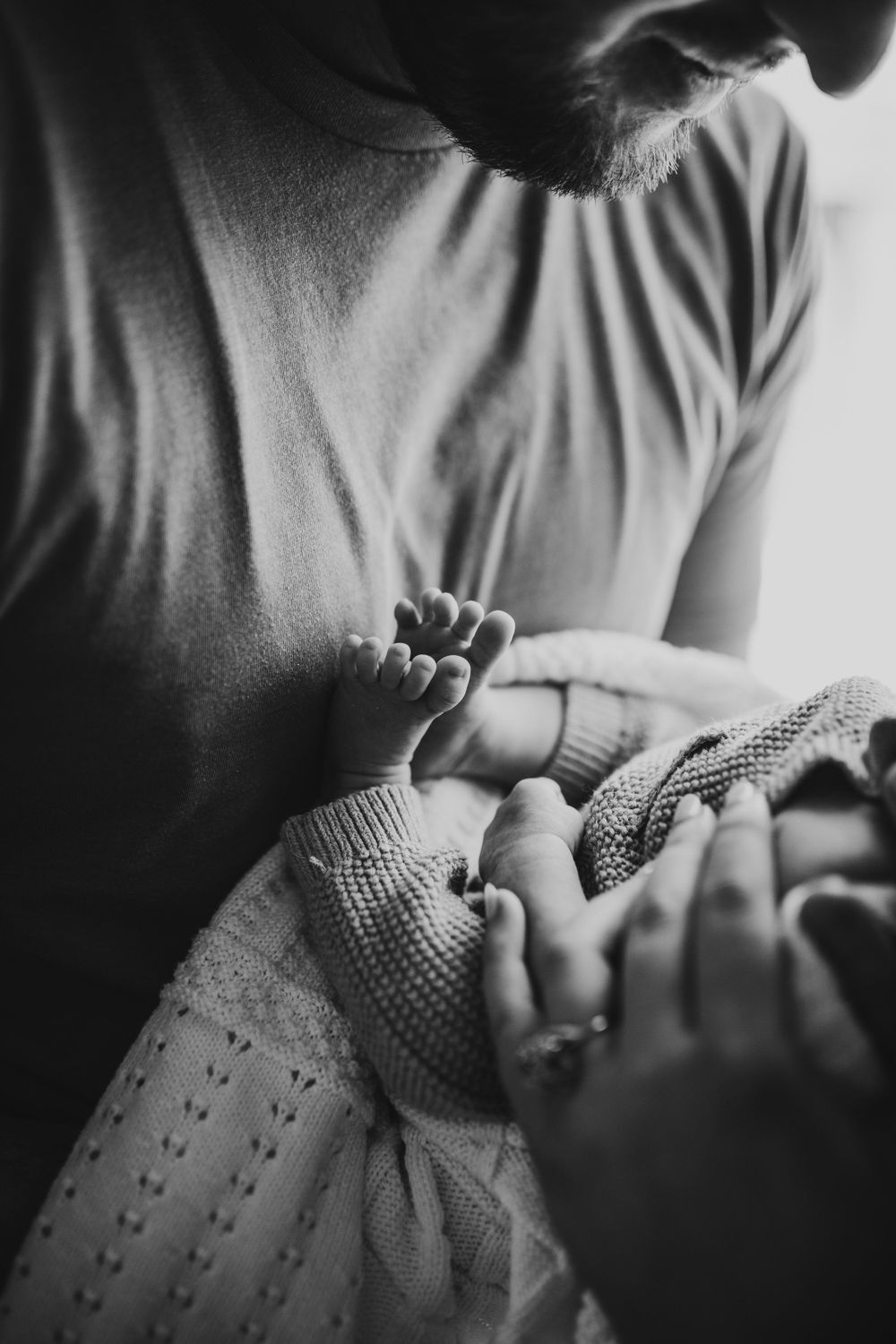 Black and white close-up of a newborns tiny feet held by parents.