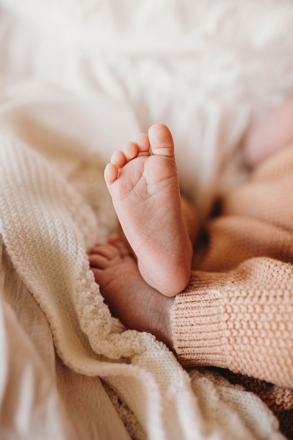 Extreme close-up of a tiny newborn baby foot peeking out from soft pink and white blankets.